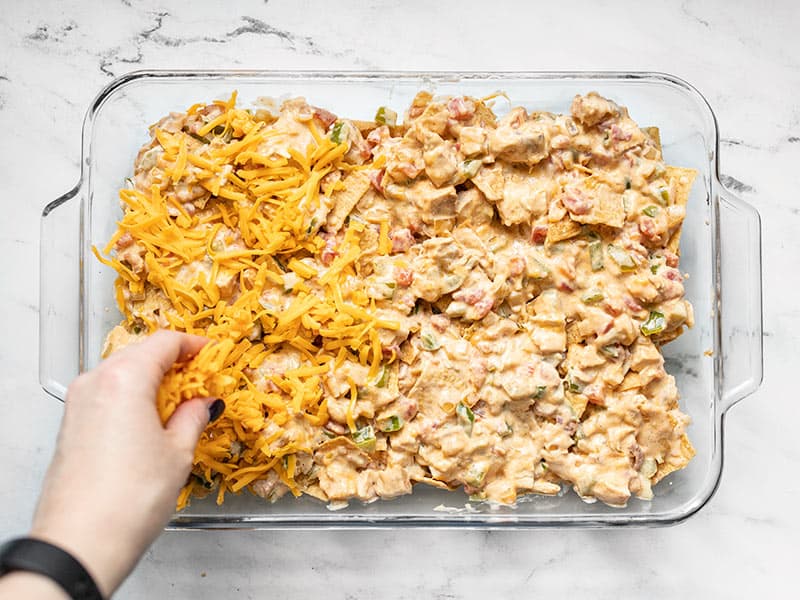 Second layer of chips and chicken mixture in casserole dish, being covered with cheese