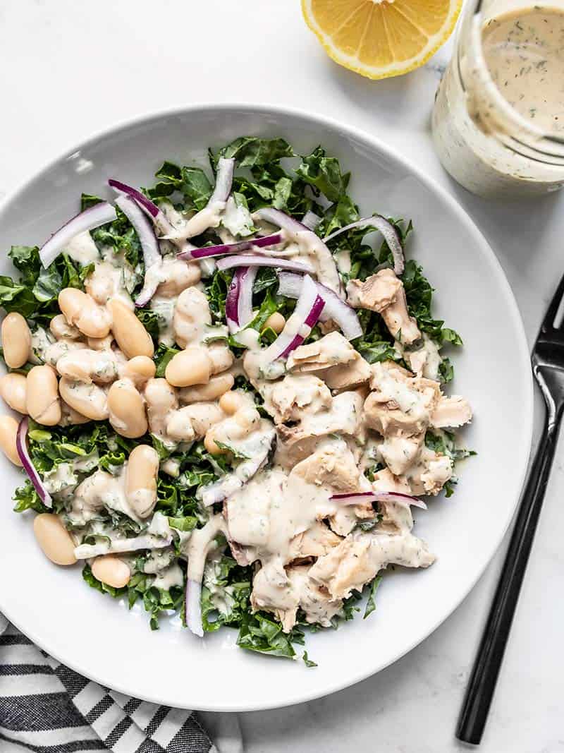 Overhead view of the Lemon Dill Salmon and Kale Salad with a jar of dressing and cut lemon on the side