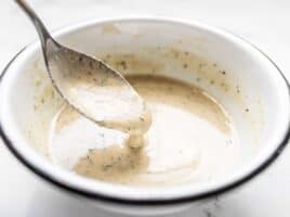 Lemon Dill Tahini Dressing dripping off a spoon into a white bowl.