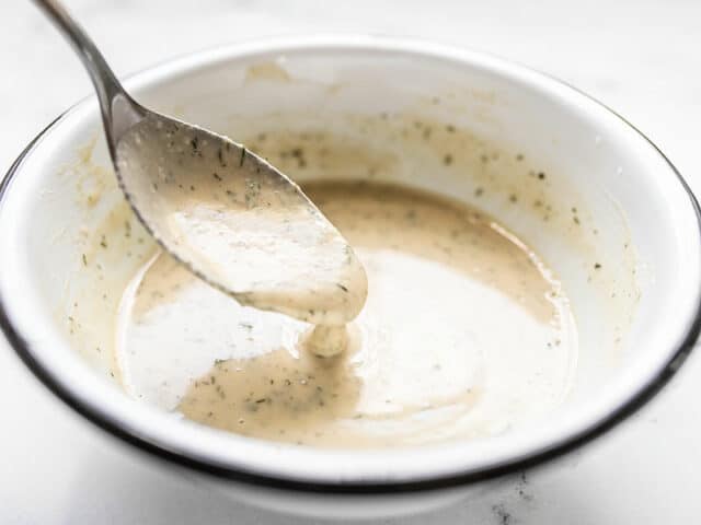 Lemon Dill Tahini Dressing dripping off a spoon into a white bowl.