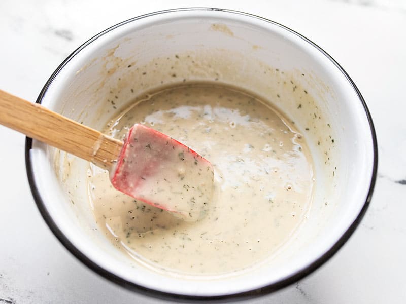 Smoothed out Lemon Dill Tahini Dressing, stirred with a red spatula.