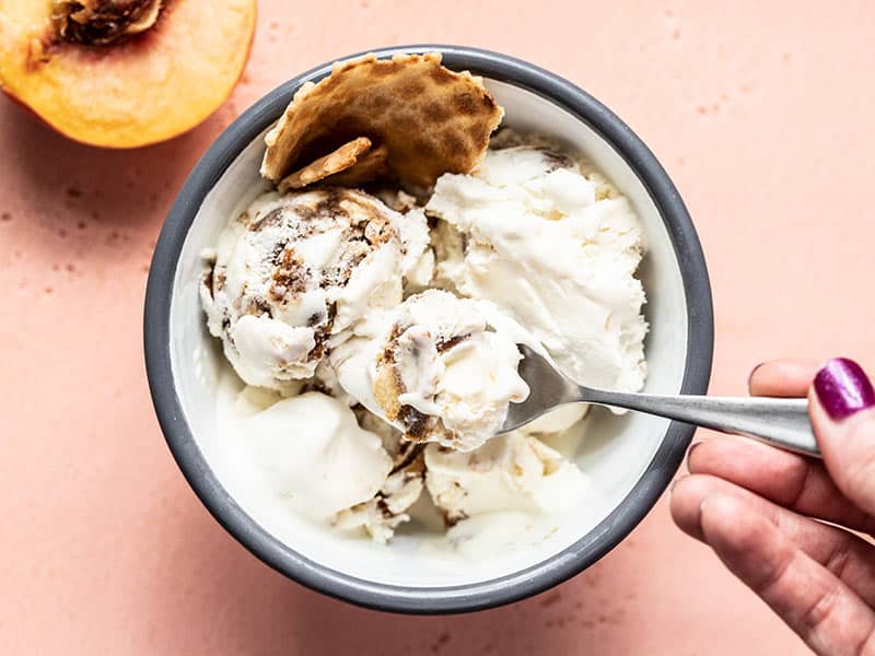 A hand lifting a spoonful of No Churn Balsamic Peach Ice Cream out of the bowl