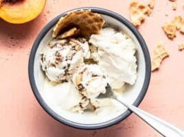 Overhead view of one bowl of no churn balsamic peach ice cream with waffle cone and a fresh peach on the side.