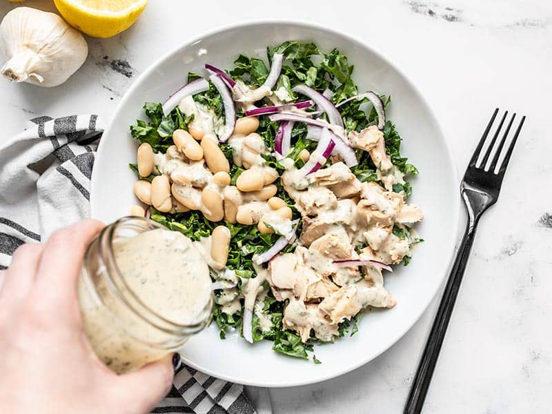 Lemon Dill Tahini Dressing being drizzled over a salmon and kale salad