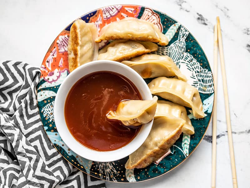 A dumpling sitting in a bowl of sweet and sour sauce, on a plate full of dumplings.