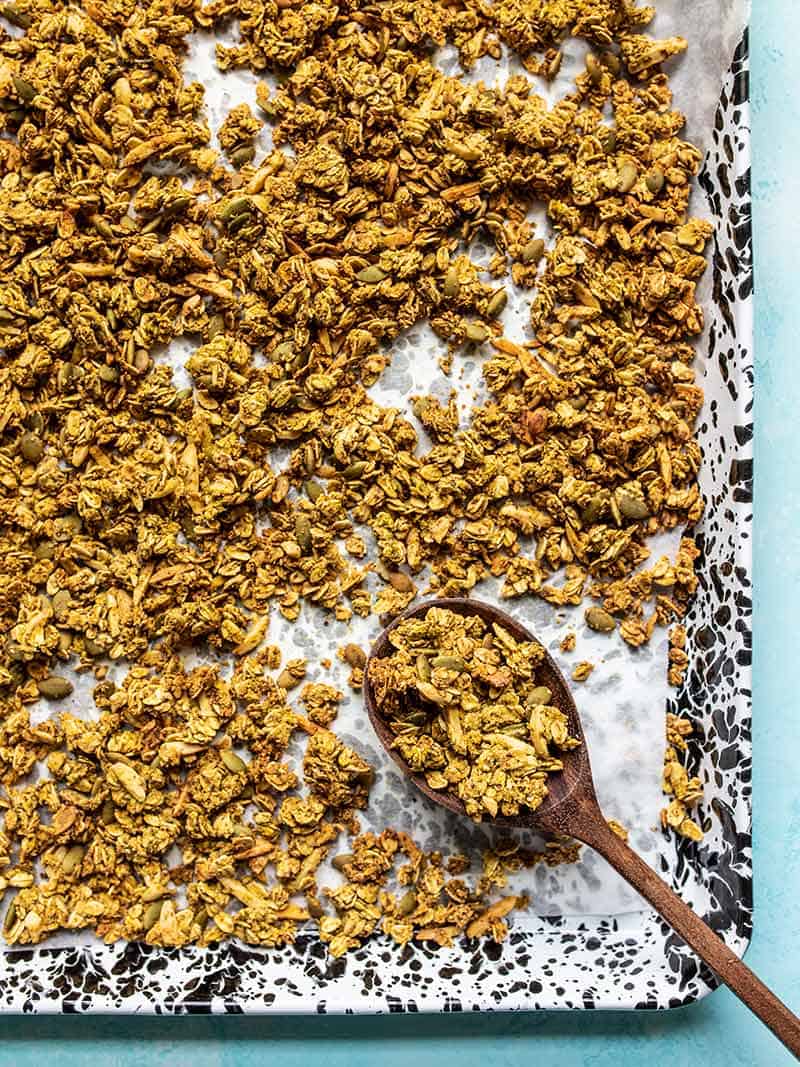 Overhead view of the tray full of Super Crunchy Oil Free Granola with a wooden spoon scooping some up in the corner.
