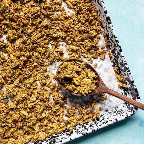 A sheet pan full of Super Crunchy Oil Free Granola with a large wooden spoon scooping it up.