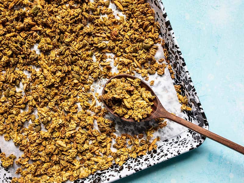 A sheet pan full of Super Crunchy Oil Free Granola with a large wooden spoon scooping it up.