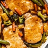 Close up overhead view of pork chops in the skillet with vegetables, covered with sweet and sour sauce.