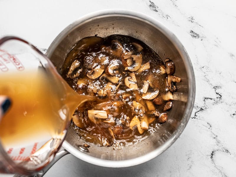 Vegetable oil being poured into the sauce pot with the cooked mushrooms