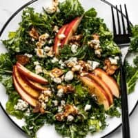 Close up overhead view of Autumn Kale and Apple Salad, with balsamic vinaigrette and a fork on the side.
