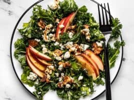 Close up overhead view of Autumn Kale and Apple Salad, with balsamic vinaigrette and a fork on the side.