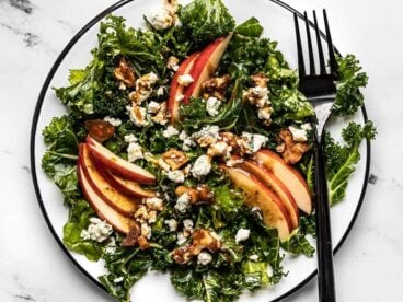 Close up overhead view of Autumn Kale and Apple Salad, with balsamic vinaigrette and a fork on the side.