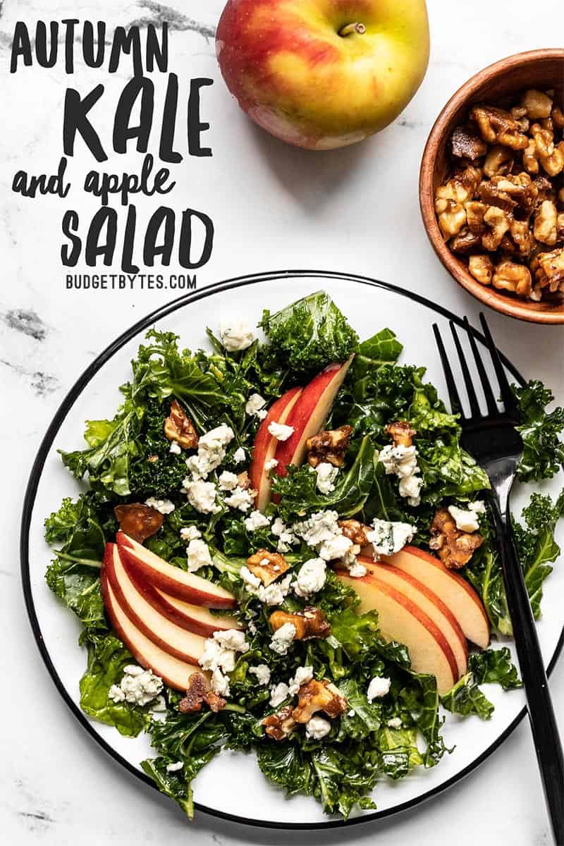 Plate of Autumn Kale and Apple Salad next to a bowl of candied walnuts and an apple