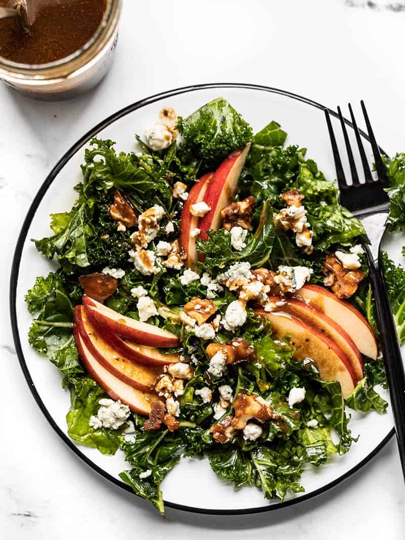 Overhead view of a plate full of Autumn Kale and Apple Salad, drizzled with balsamic vinaigrette and a black fork on the side of the plate.