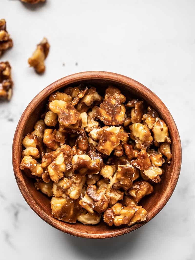 A small wooden bowl full of chopped crunchy candied walnuts