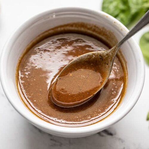 A spoon lifting some homemade balsamic vinaigrette out of a small bowl
