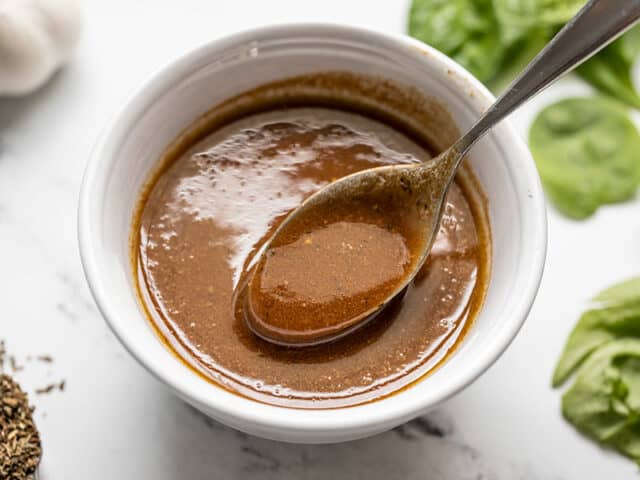 A spoon lifting some homemade balsamic vinaigrette out of a small bowl