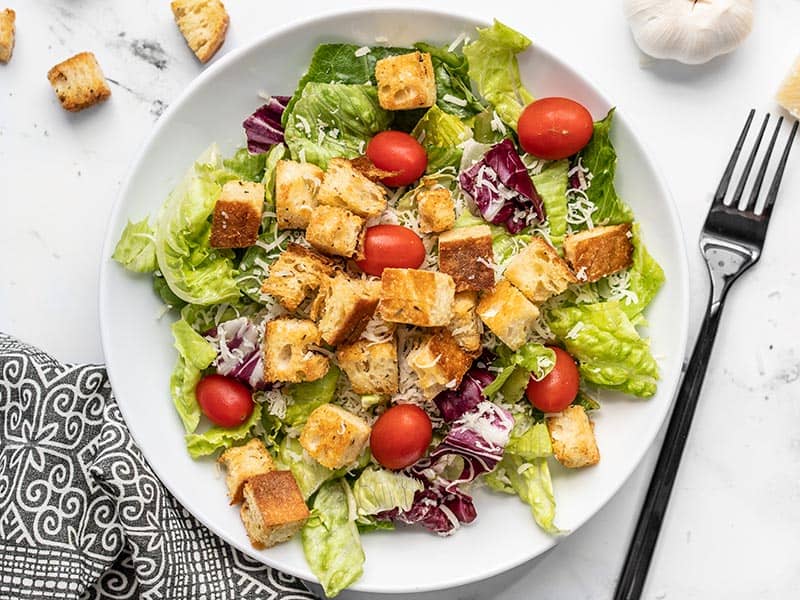 Overhead view of a large salad bowl with easy homemade baked croutons, Parmesan, and tomatoes.