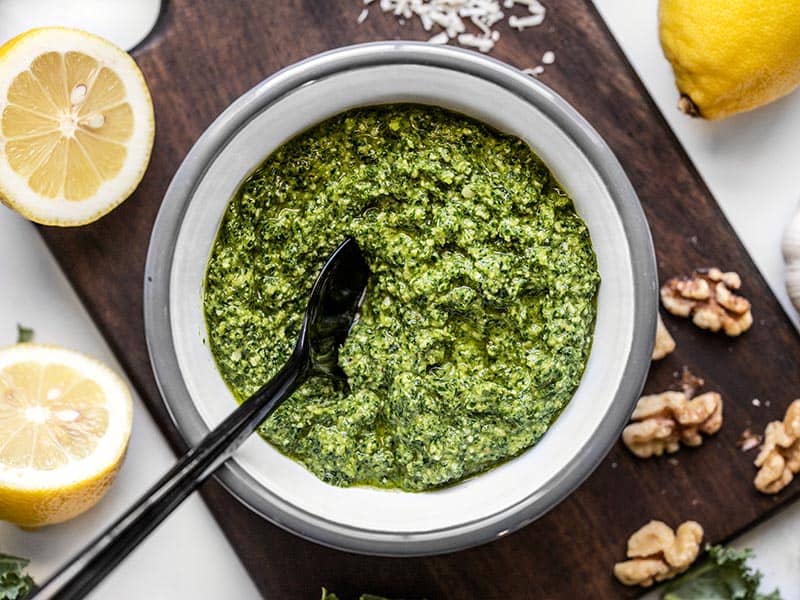 Overhead view of a bowl full of kale pesto with a black spoon in the middle