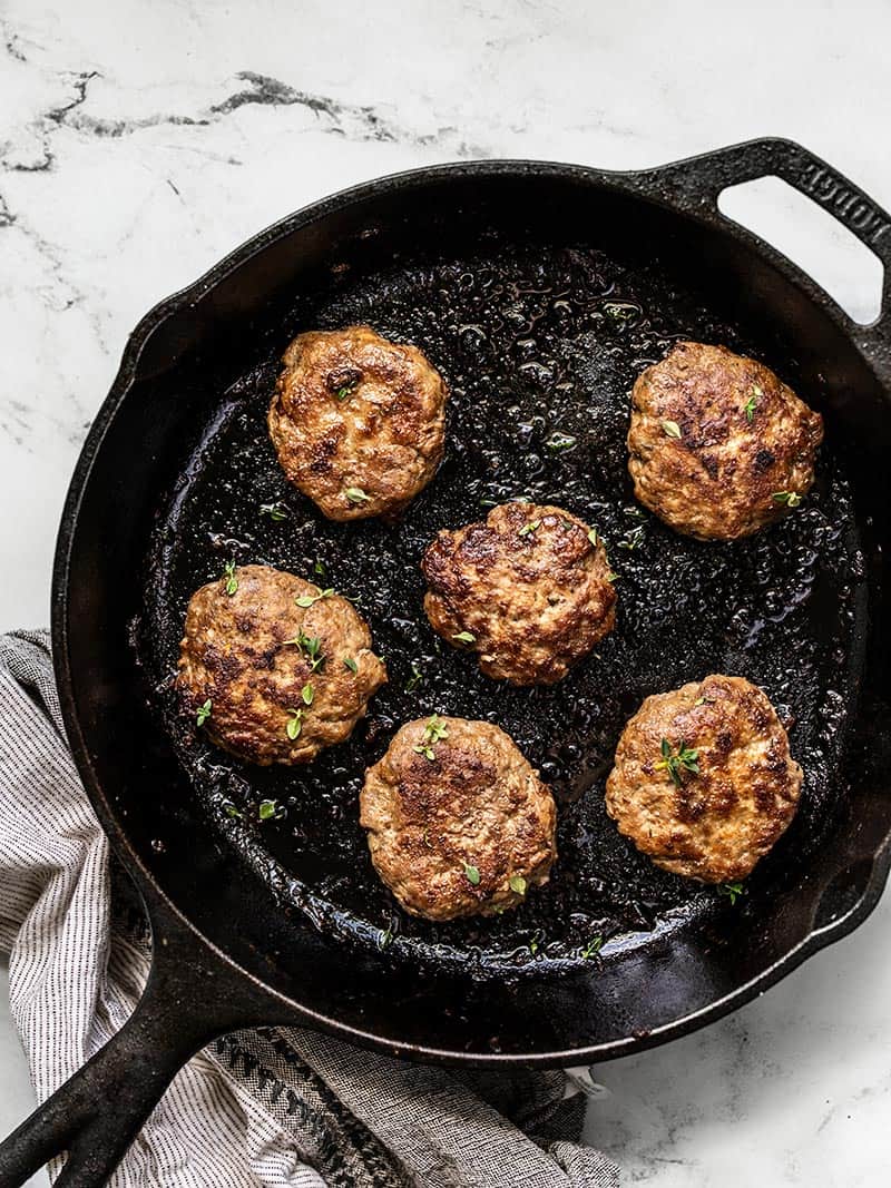 Overhead of a cast iron skillet with five cooked Maple Sage Breakfast Sausage patties