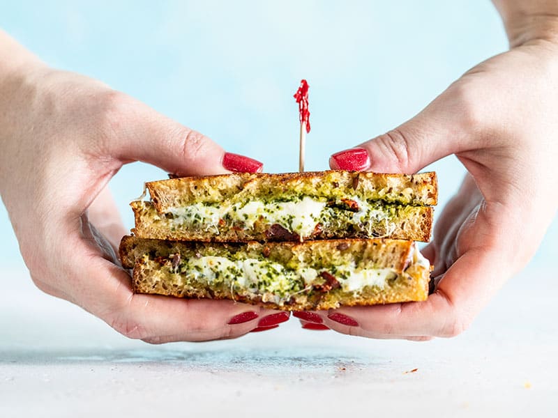 Hands holding a stacked pesto grilled cheese facing the camera.