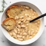 A bowl of Rosemary Garlic White Bean Soup with two pieces of toasted bread and a black spoon in the middle.