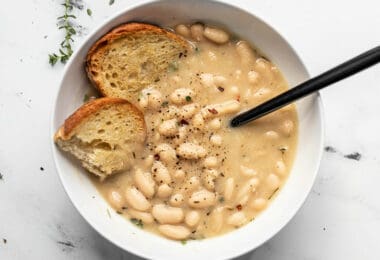 A bowl of Rosemary Garlic White Bean Soup with two pieces of toasted bread and a black spoon in the middle.