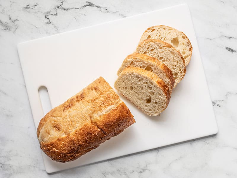 Four slices of French Bread on a cutting board next to the rest of the loaf.