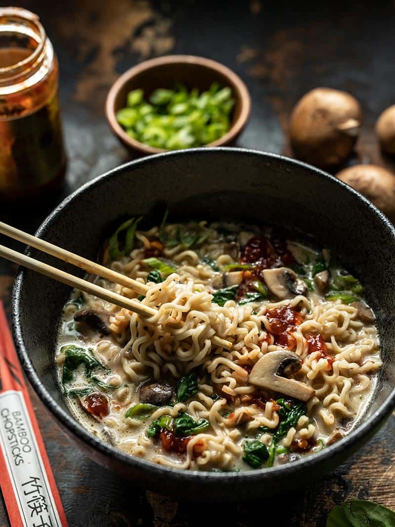 Noodles being lifted by chopsticks out of a black bowl full of vegan creamy mushroom ramen