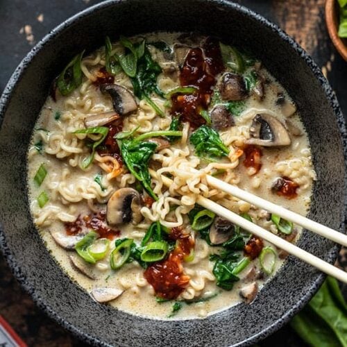 Close up overhead view of a bowl full of vegan creamy mushroom ramen with chopsticks lifting some noodles