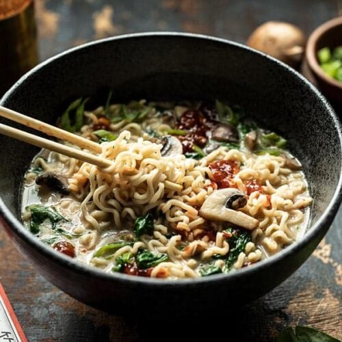 Front view of noodles being lifted out of a bowl of vegan creamy mushroom ramen with chopsticks