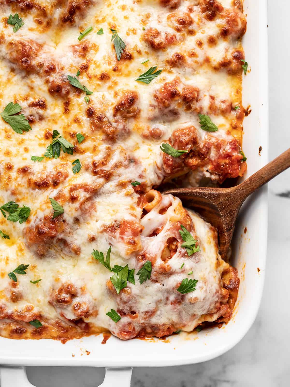 Overhead view of baked ziti being scooped out of the casserole dish.