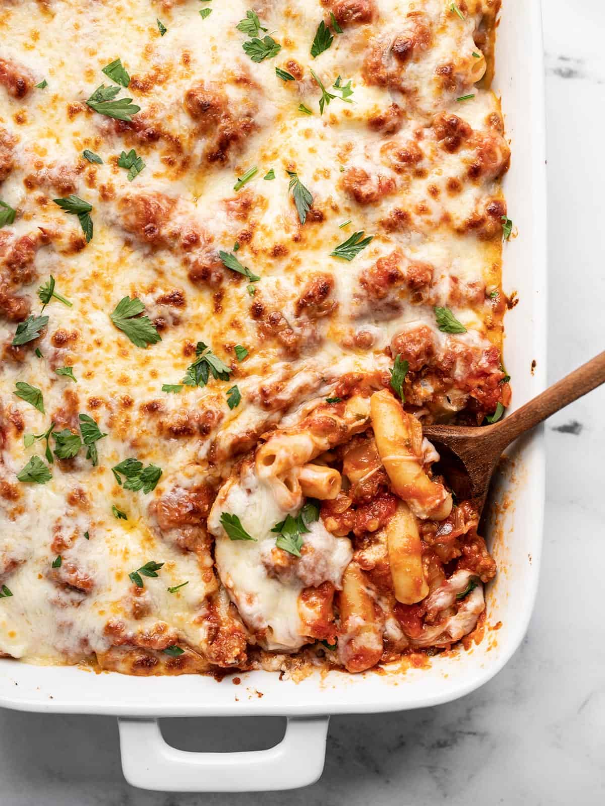 Overhead view of a casserole dish full of baked ziti with the corner being scooped out.