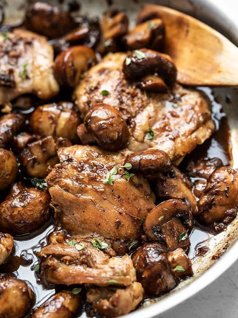 Close up side view of finished balsamic chicken and mushrooms in the skillet with a wooden spoon