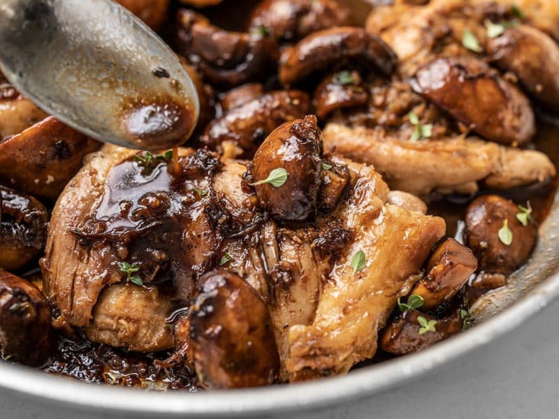 Close up of the balsamic pan sauce being drizzled over the chicken and mushrooms in the skillet