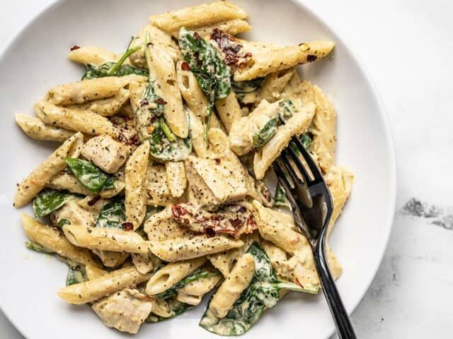 Close up of one pot creamy pesto chicken pasta in a shallow bowl with a black fork.