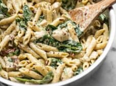 Close up of One Pot Creamy Pesto Chicken Pasta in the skillet with a wooden spoon.
