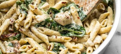 Close up of One Pot Creamy Pesto Chicken Pasta in the skillet with a wooden spoon.