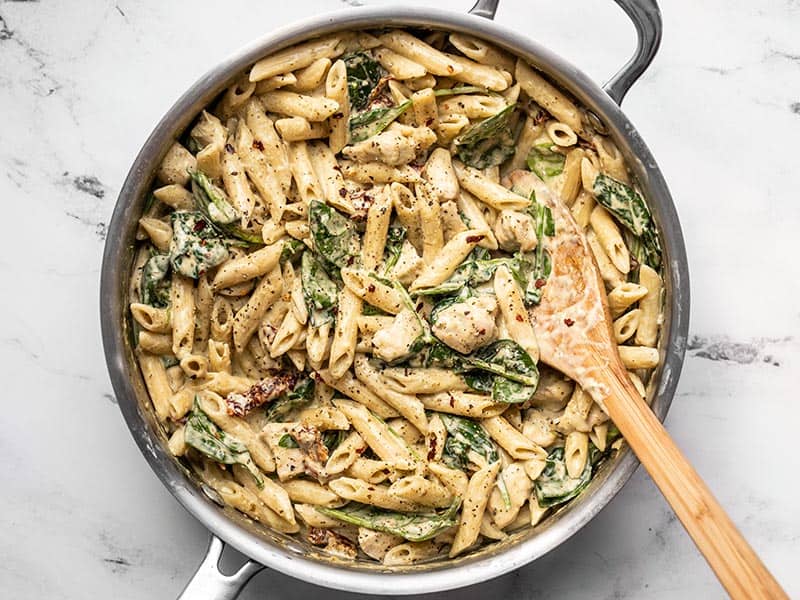 Finished creamy pesto chicken pasta in the skillet topped with black pepper and crushed red pepper