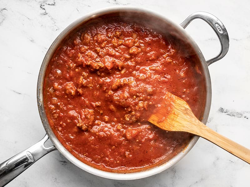 Red meat sauce in a skillet with a wooden spatula