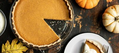 Overhead view of a Maple Brown Butter Pumpkin Pie with a slice cut out, on a plate on the side with whipped cream.