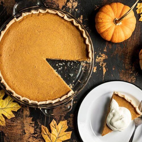 Overhead view of a Maple Brown Butter Pumpkin Pie with a slice cut out, on a plate on the side with whipped cream.