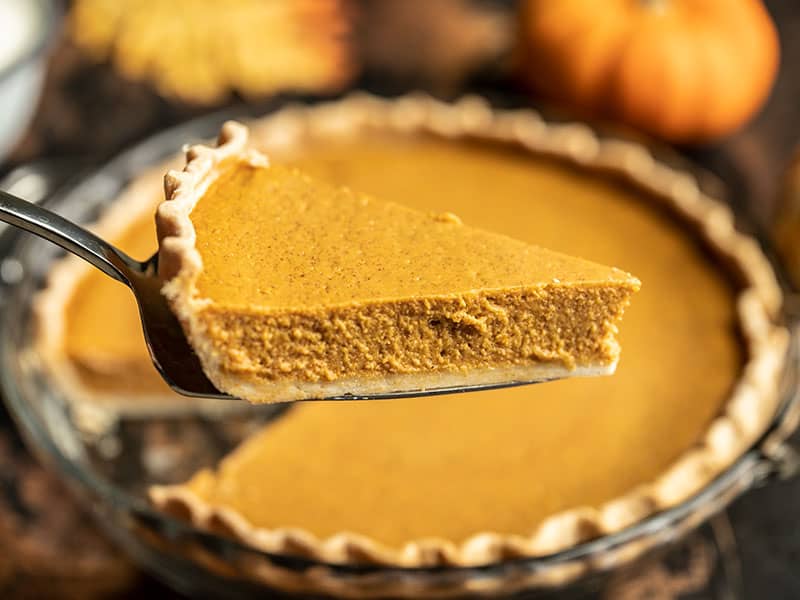 A slice of Maple Brown Butter Pumpkin Pie close to the camera, whole pie in the background.