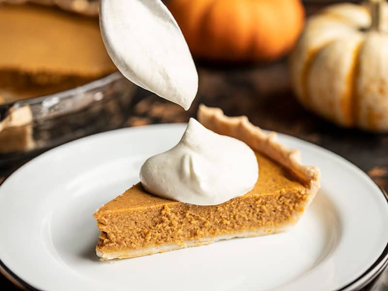 Whipped cream being scooped onto a slice of Maple Brown Butter Pumpkin Pie