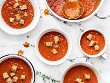 Five different bowls full of tomato soup with the soup pot and ladle at the top