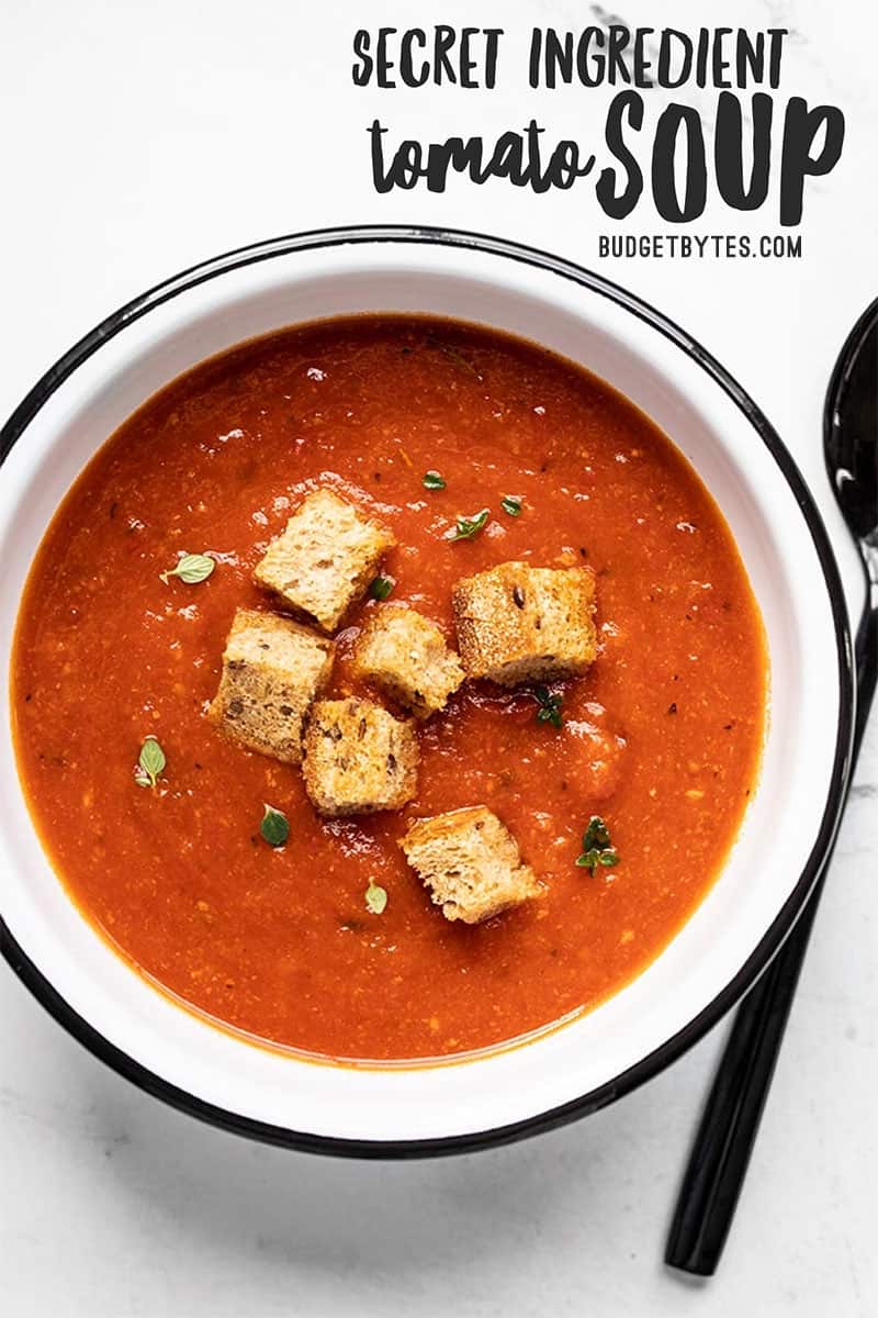 Overhead view of a white bowl full of secret ingredient tomato soup with title text overlay at the top.