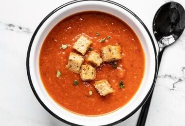 Overhead view of secret ingredient tomato soup in a white bowl with black rim, and a black spoon.