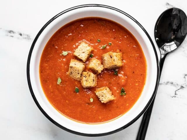 Overhead view of secret ingredient tomato soup in a white bowl with black rim, and a black spoon.