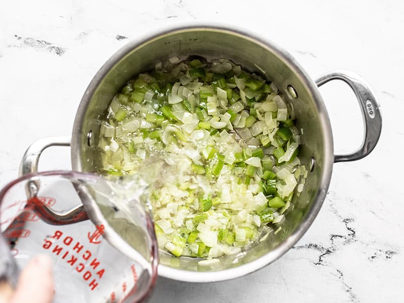 Water being poured into a pot with sautéed onion and celery 